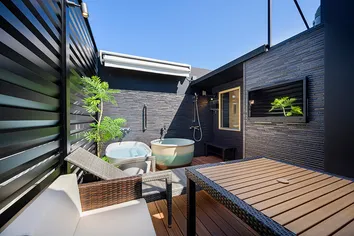 青空の下に設置された外気浴テラス。2つの水風呂、リクライニングチェア、ラタン調のテーブルセットが配置された開放的な空間